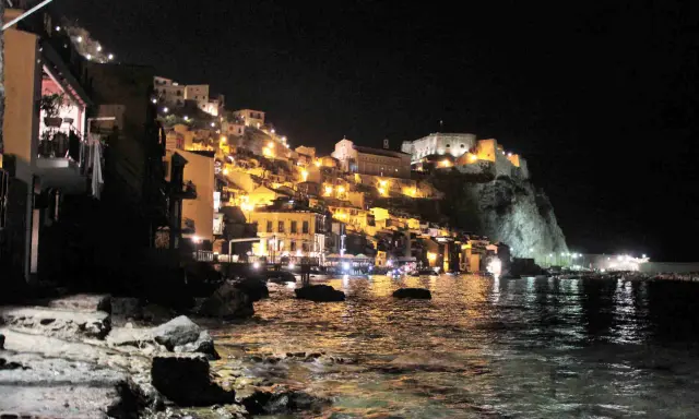 Scilla illuminata di notte, un incanto da visitare a piedi. Case colorate e il castello arroccato sul promontorio si specchiano nel mare.