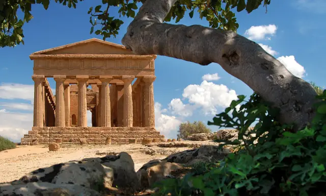 Tempio greco dorico, parte del patrimonio UNESCO Sicilia, si staglia sotto un cielo azzurro con nuvole bianche.