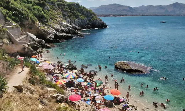 Affollata baia dei Francesi con gente che prende il sole e nuota nelle acque cristalline.