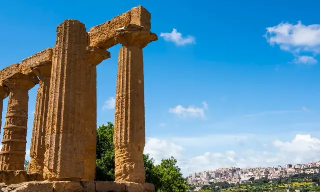 Colonne doriche imponenti, testimoni del **significato** di Akragas, con una città moderna sullo sfondo.