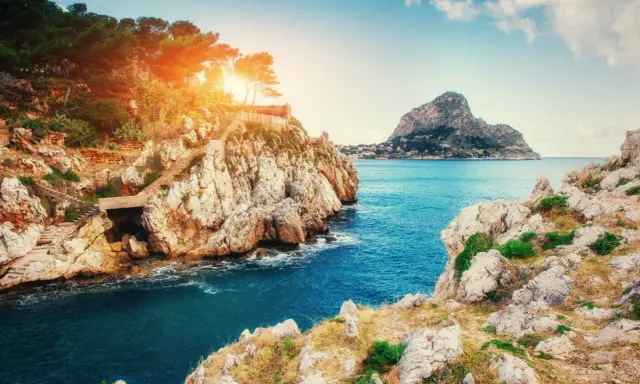 Scogliere rocciose e mare blu intenso vicino a Milazzo, con sentieri che scendono verso l'acqua. Le spiagge di Milazzo offrono panorami mozzafiato.