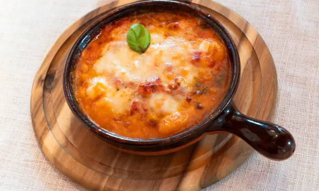 Piatto fumante di gnocchi al forno, uno dei piatti tipici della Campania, con pomodoro e mozzarella filante, guarnito con basilico.