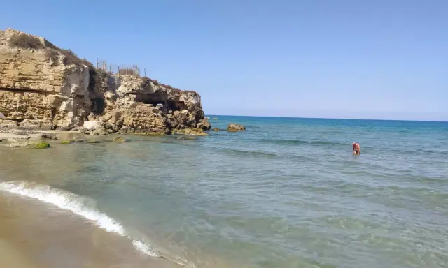 Spiaggia di Eloro con scogliere rocciose, mare azzurro e una persona che fa il bagno.