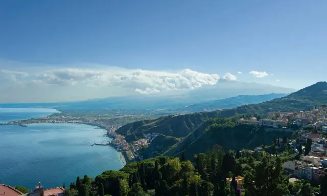 Vista panoramica della costa siciliana con il mare blu, la città di Taormina e l'Etna sullo sfondo. Un luogo incantevole, quasi un casinò di Taormina naturale.