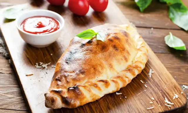 Un dorato cudduruni palermitano, guarnito con basilico, su tagliere di legno, con pomodorini e salsa di pomodoro.