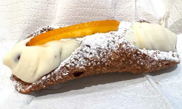 Cannolo ripieno di ricotta, uno dei dolci tipici di Palermo, cosparso di zucchero a velo e decorato con scorza d'arancia candita.