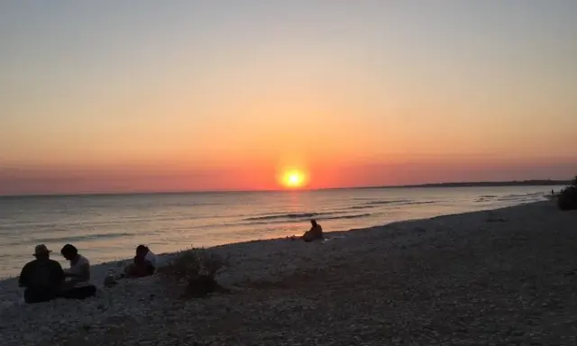Tramonto sulle menfi spiagge più belle. Persone sedute sulla riva, godendosi la vista del sole che cala sul mare.