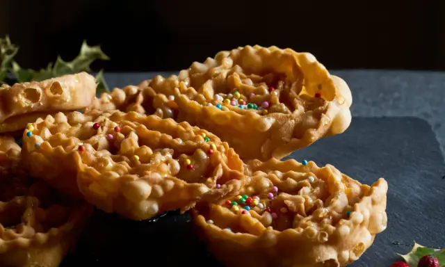 Cartellate, dolci tipici della Puglia, ricoperte di miele e confettini colorati, con un rametto di agrifoglio sullo sfondo.