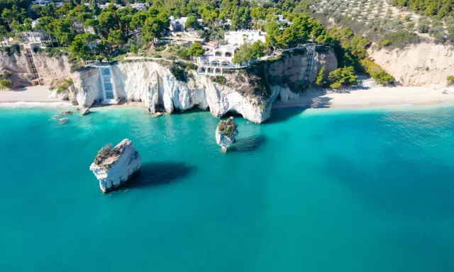 Scogliere bianche a picco sul mare turchese, con rocce isolate e vegetazione lussureggiante. Un vero angolo di paradiso tra le spiagge più belle della Puglia.
