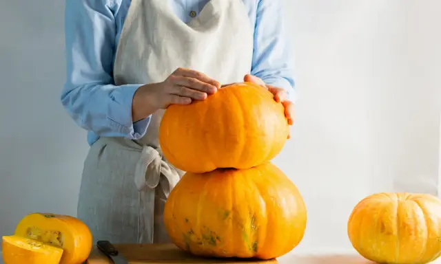 Mani che impilano zucche arancioni, una tagliata a metà su un tagliere. La cucuzza baffa è pronta per essere preparata.
