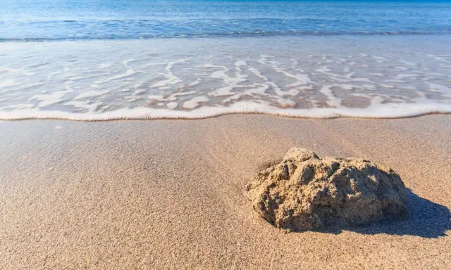 Onda che lambisce la sabbia dorata della spiaggia Tonnarella Mazara, con una roccia in primo piano.