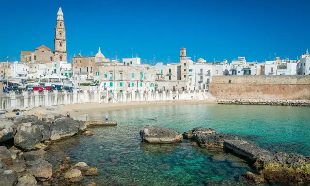 Vista del lungomare di Monopoli con case bianche, una torre campanaria e il mare cristallino. Perfetto per scoprire le cose da fare a Monopoli.