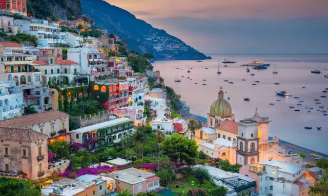 Vista mozzafiato dal **punto panoramico Positano**, con case colorate aggrappate alla scogliera e barche nel mare al tramonto.