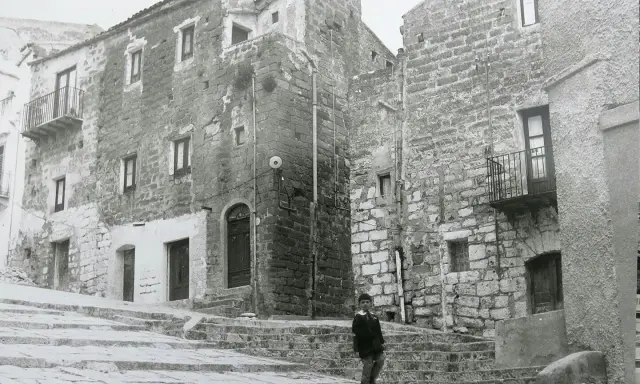 Un bambino cammina su una scalinata di pietra a Gibellina prima del terremoto. Edifici antichi in pietra la circondano.