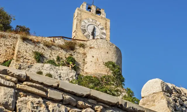La torre dell'orologio di Modica, con il suo quadrante romano, domina il paesaggio sotto un cielo azzurro.