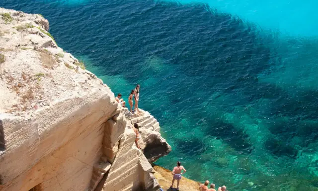 Persone si godono le splendide spiagge di Favignana, tuffandosi da scogliere in acque cristalline.