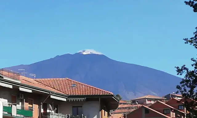 Vista dell'Etna fumante, un'imponente montagna che domina il paesaggio. Un'ottima meta per scoprire cosa vedere a Bronte, con i suoi tetti rossi in primo piano.