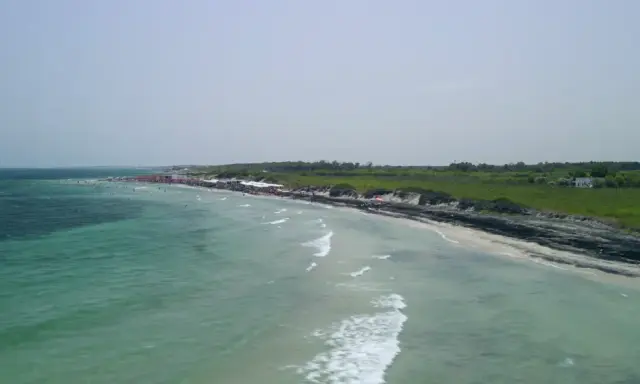Vista aerea del lido Le Cesine, con acque turchesi e una spiaggia affollata di bagnanti e ombrelloni rossi.