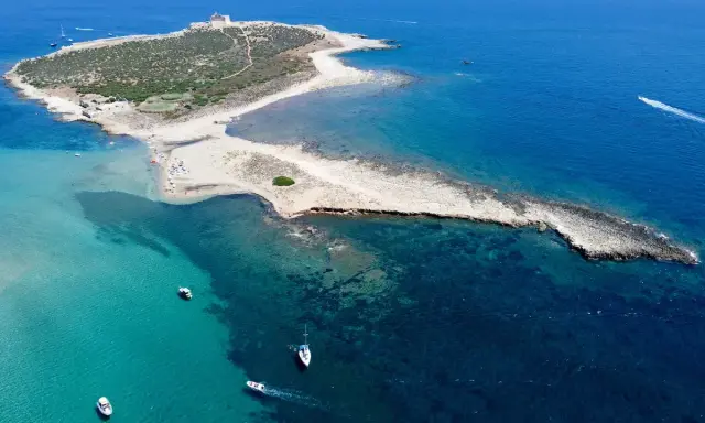 L'isola delle Correnti, leggenda di sabbia e mare cristallino, con un faro bianco e barche che solcano le acque turchesi.