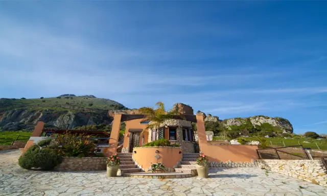 Il castello di Baida, con la sua architettura unica, si erge su un terreno roccioso sotto un cielo azzurro.