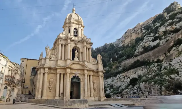 La chiesa barocca di San Giuseppe a Scicli, con il suo Cristo in gonnella, si erge maestosa contro una scogliera rocciosa.