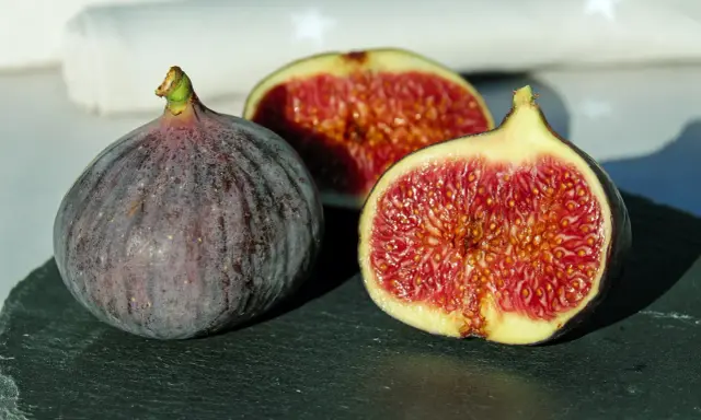 Un intero fico viola e due metà succose rivelano la dolcezza di una varietà di fichi siciliani, con la loro polpa rossa e i semi dorati.