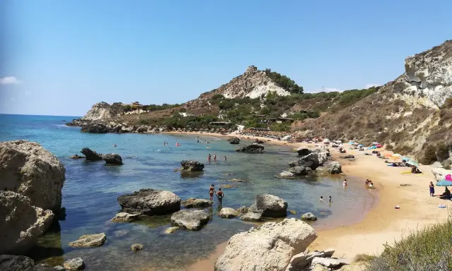 Splendida spiaggia la rocca licata con acque cristalline e scogliere rocciose. Turisti si godono il sole e il mare.