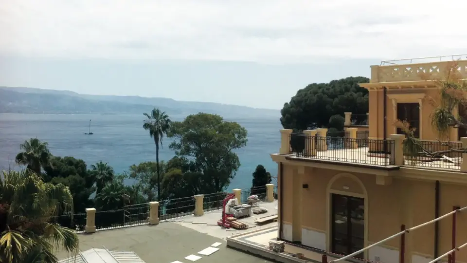 Vista mare dalla villa Bosurgi a Messina, con alberi tropicali e un veliero all'orizzonte.