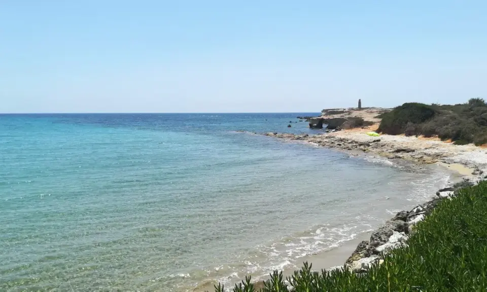 Acque cristalline e scogliere rocciose sulla spiaggia delle Formiche, Portopalo di Capo Passero. Un faro solitario veglia sul mare.