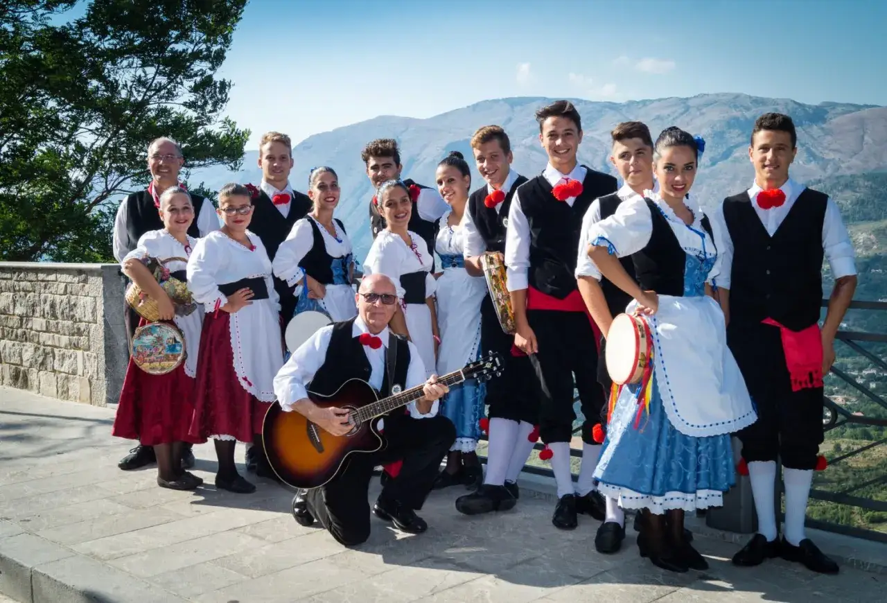 Un gruppo di persone in abiti tradizionali siciliani, pronti a intonare canzoni siciliane famose con chitarra e tamburello.