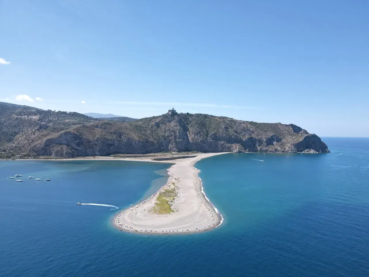 Spiaggia a forma di mezzaluna nei laghetti di Marinello, dove si può fare il bagno. Montagne verdi sullo sfondo e mare azzurro.