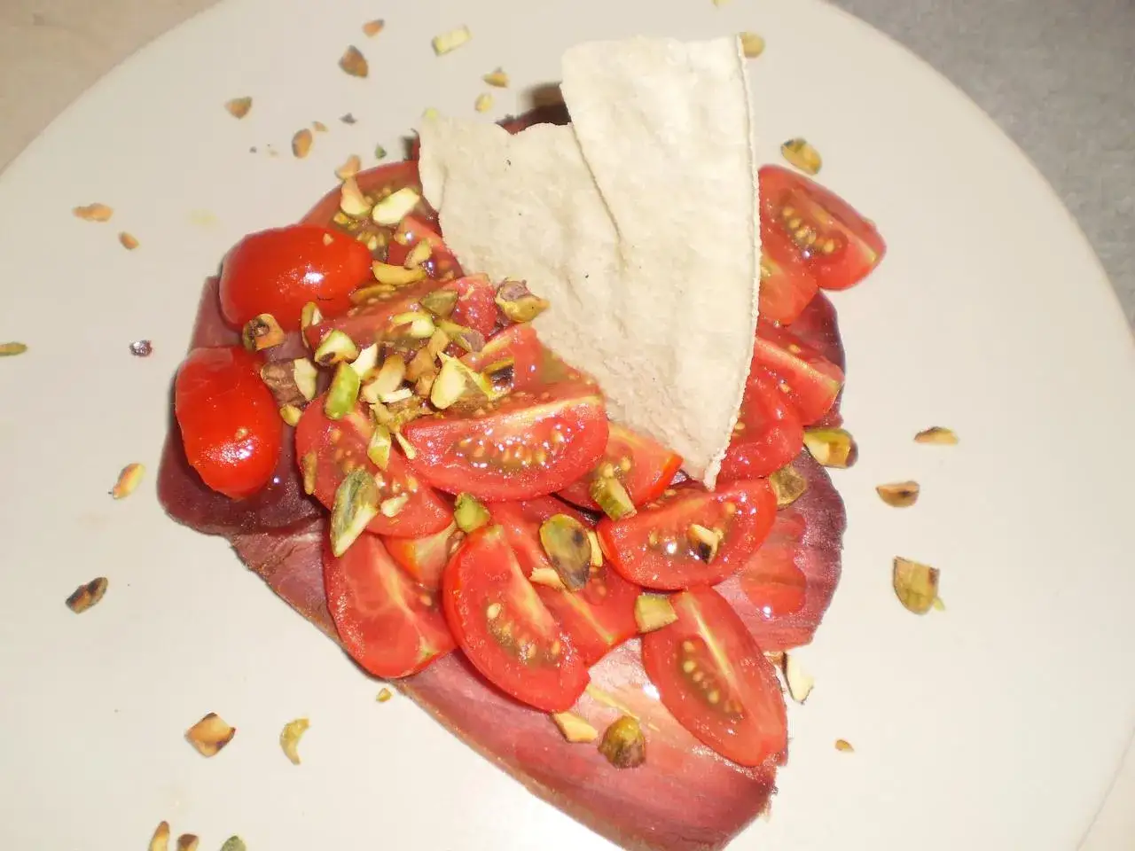 Un piatto con mosciame di tonno, pomodorini, pistacchi tritati e una cialda croccante. Un assaggio di mare e terra.