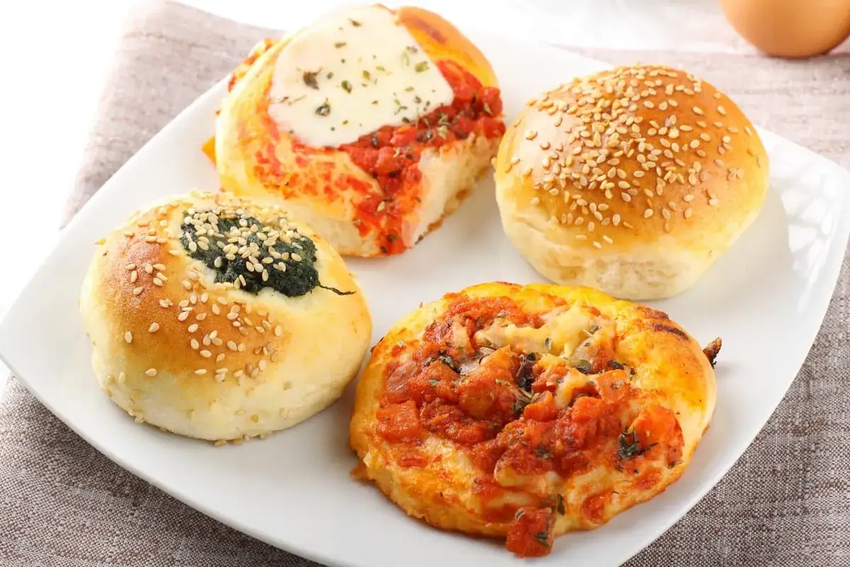 Piatto con specialit&agrave; siciliane salate: focaccine con pomodoro, mozzarella e spinaci, cosparse di semi di sesamo.