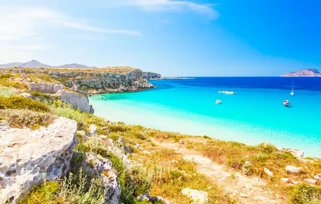Favignana spiagge: acque cristalline e scogliere rocciose, un paradiso mediterraneo con barche all'orizzonte.
