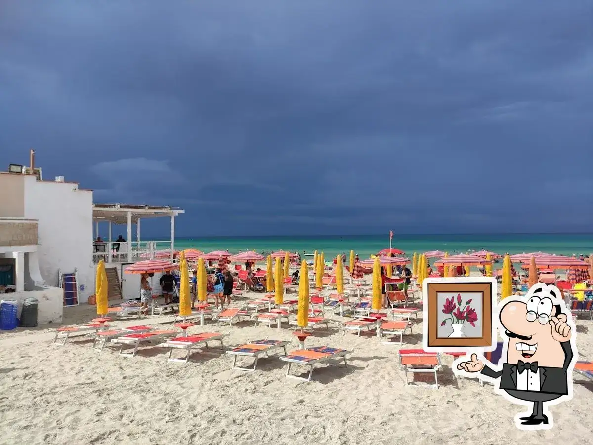 Lido Circeo Torre Chianca: ombrelloni rossi e gialli, lettini pronti per i bagnanti, con un cielo minaccioso all'orizzonte.