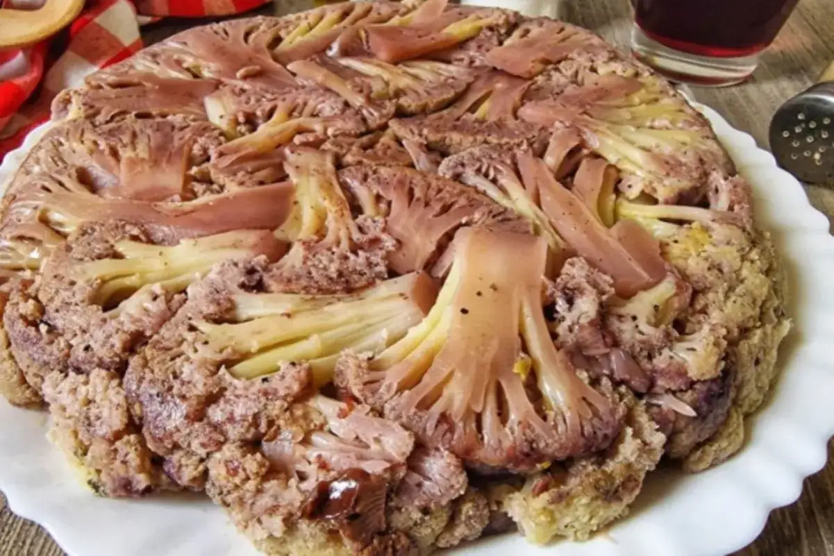Cavolfiore intero cotto al forno, con fette di prosciutto e spezie. Sembra delizioso, quasi dei bastardi affucati.