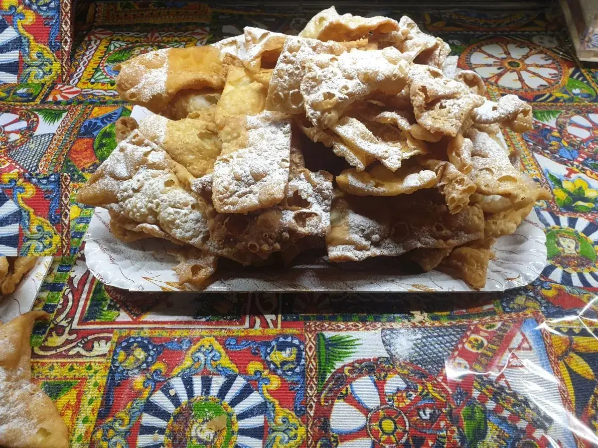 Dolci fritti cosparsi di zucchero a velo, un assaggio di cosa si mangia in Sicilia, su un colorato sfondo decorato.