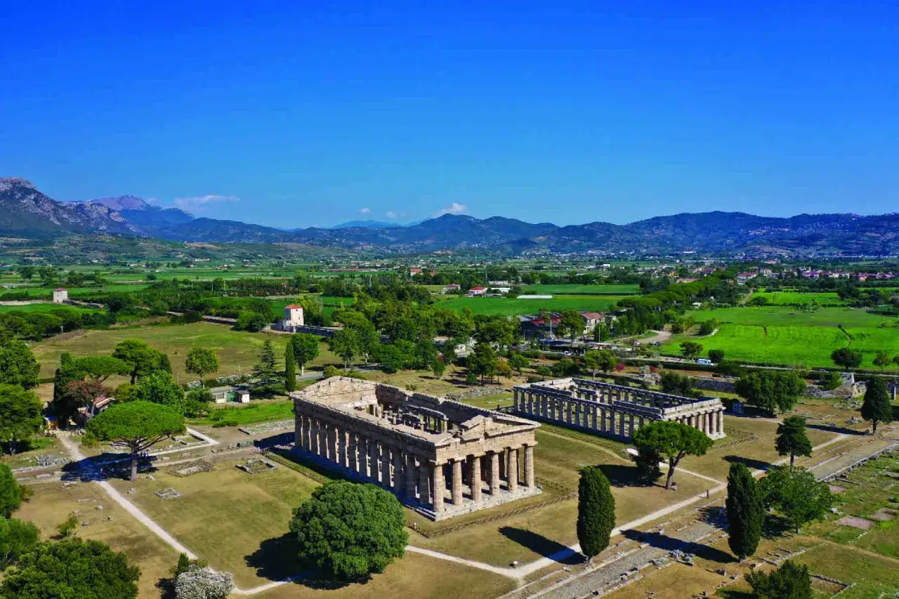 Antichi templi dorici di Magna Grecia a Paestum, con montagne sullo sfondo e campi verdi.