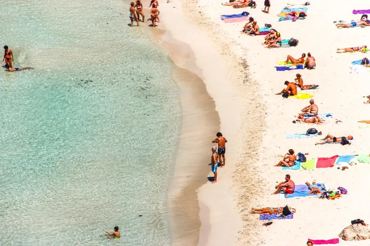 Spiaggia affollata, bagnanti prendono il sole e nuotano. Forse si chiama isola dei conigli per la sua bellezza selvaggia e incontaminata.