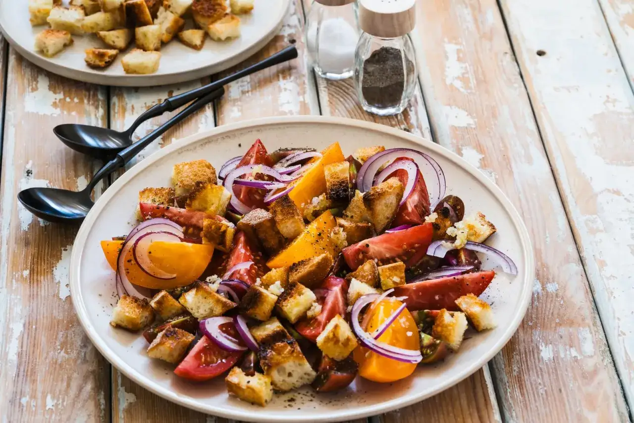 Un piatto di panzanella siciliana con pomodori, cipolla rossa e crostini croccanti.