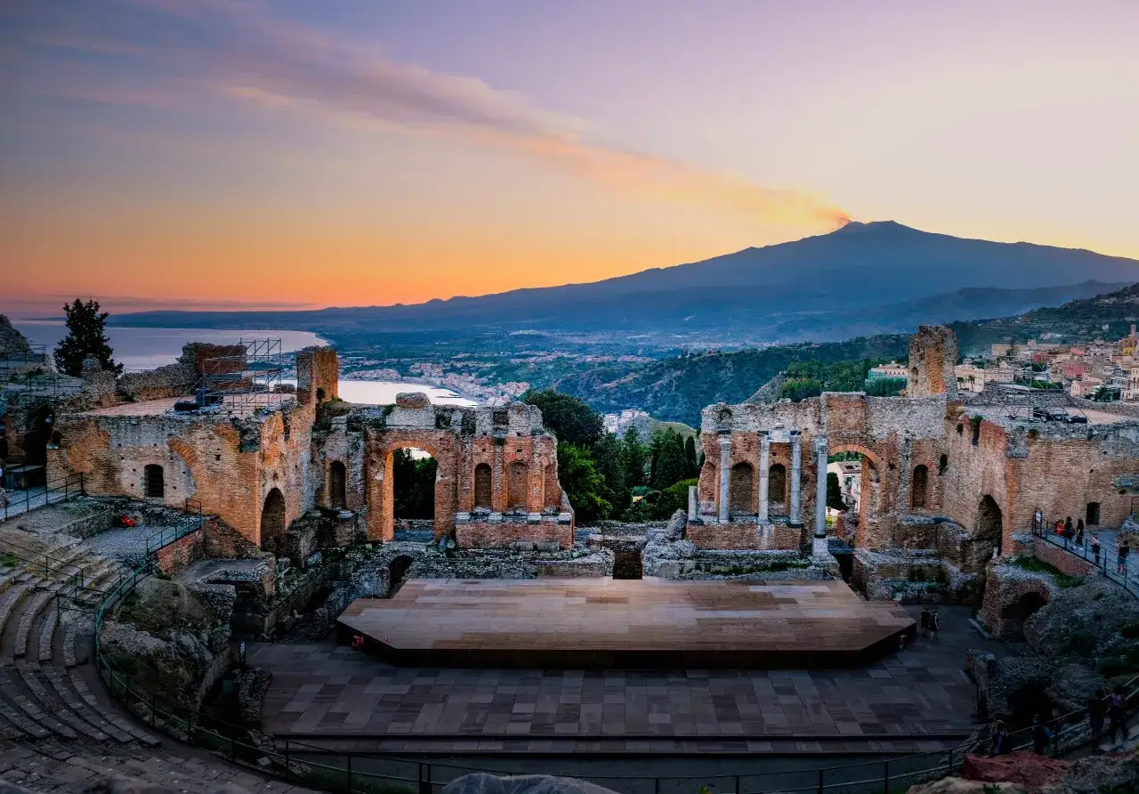 Teatro antico di Taormina con vista sull'Etna fumante al tramonto, un luogo magico tra Giardini Naxos e Taormina.
