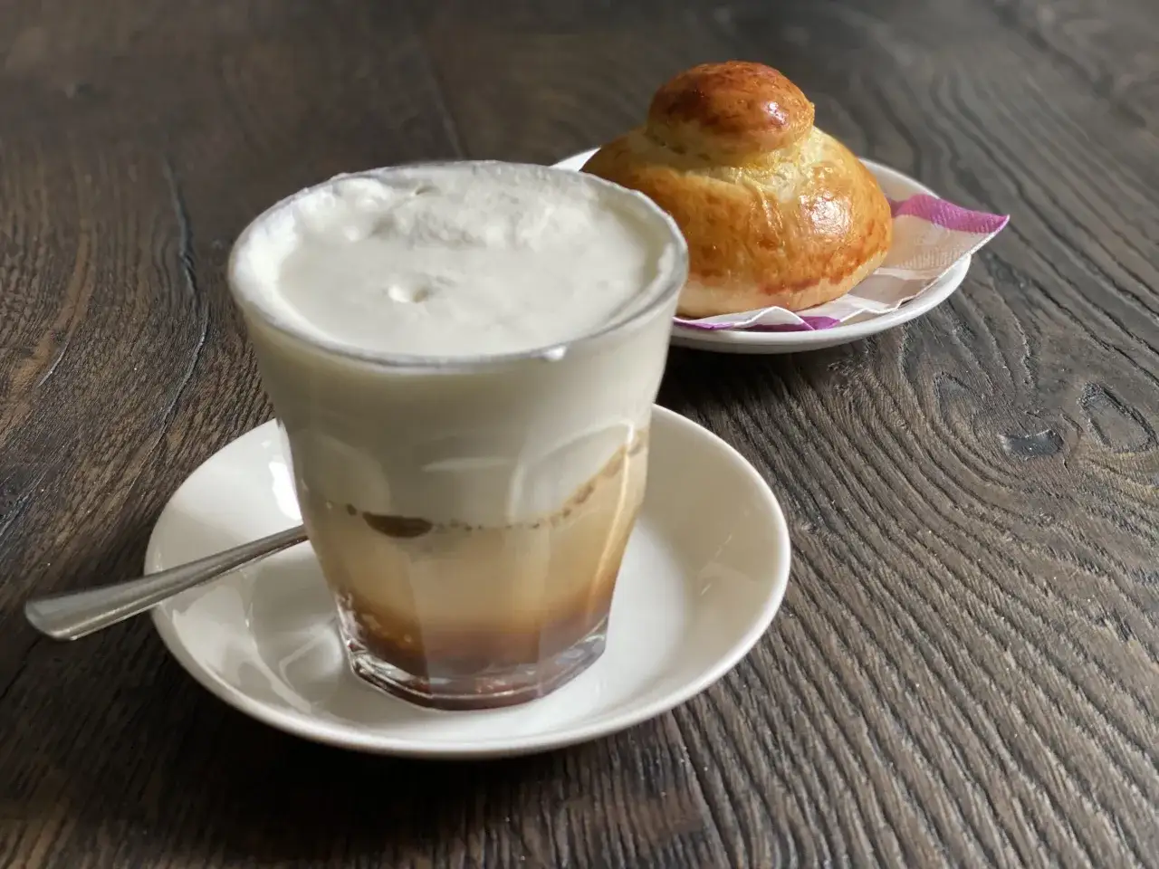 Un bicchiere di caffè freddo siciliano con panna montata e una brioche soffice su un piattino, su un tavolo di legno scuro.