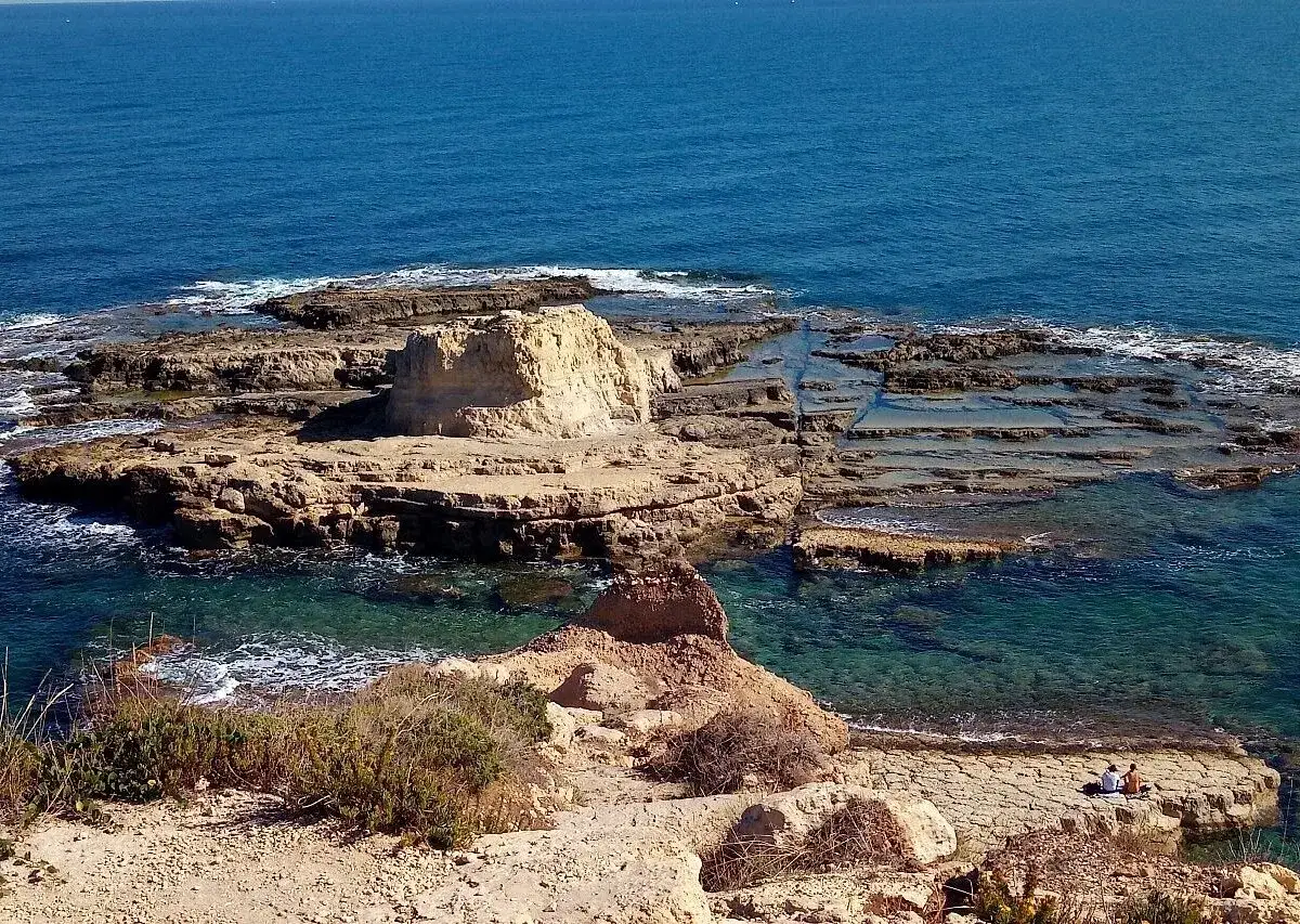 Scogliera rocciosa con acqua cristallina, dove si narra avvenne lo sbarco dei turchi. Due persone sedute ammirano il panorama.