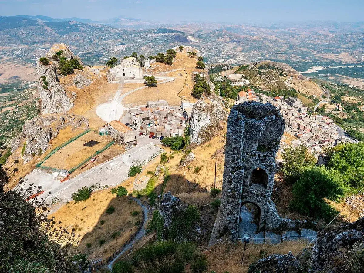 Rovine di un'antica torre del castello di Baida dominano un villaggio arroccato su una montagna, con una chiesa in cima.