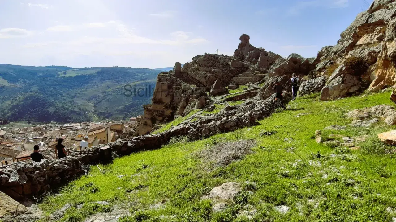 Caltavuturo cosa vedere: sentiero roccioso con antiche scale conduce a un sito archeologico, con vista panoramica sul borgo e sulle colline siciliane.