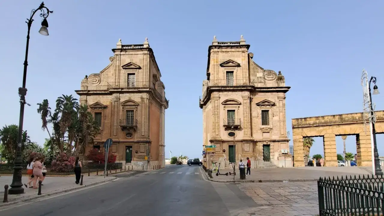 Due palazzi gemelli affiancano la strada, con un arco in pietra sullo sfondo. La porta del sole a Palermo, un luogo iconico.