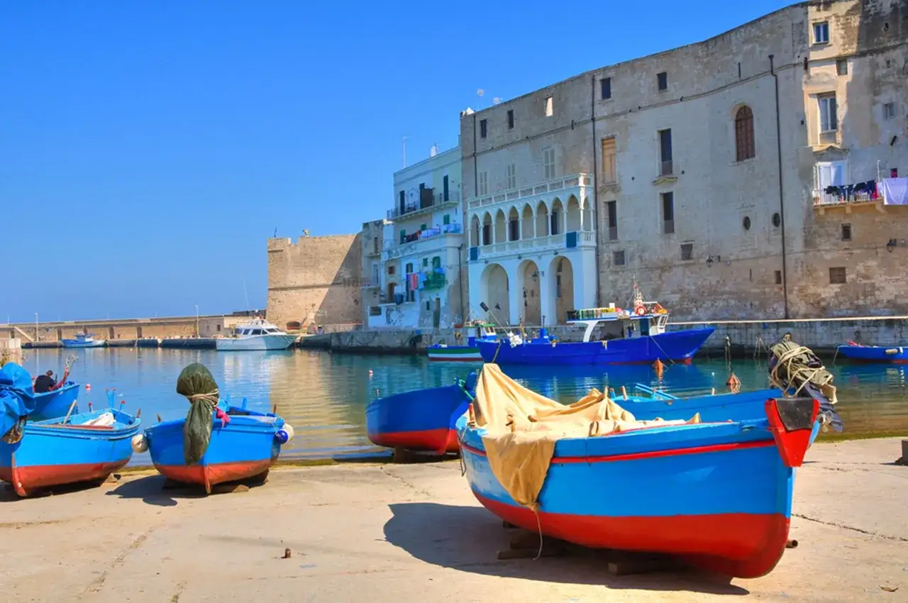 Barche blu e rosse ormeggiate nel porto di Monopoli, con edifici storici sullo sfondo. Un'ottima immagine per scoprire le cose da fare a Monopoli.