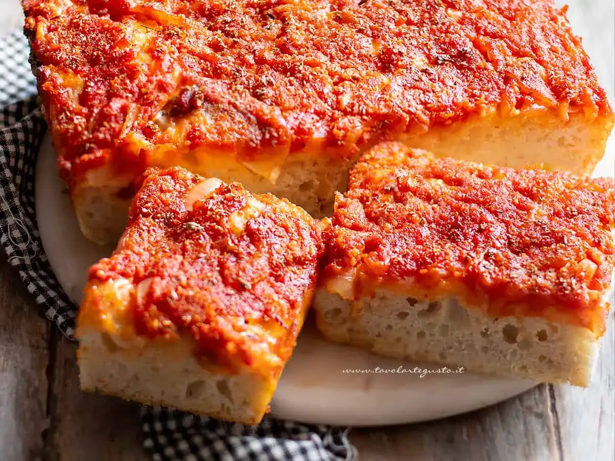 Fetta di cudduruni palermitano, soffice focaccia con pomodoro e formaggio, pronta per essere gustata.
