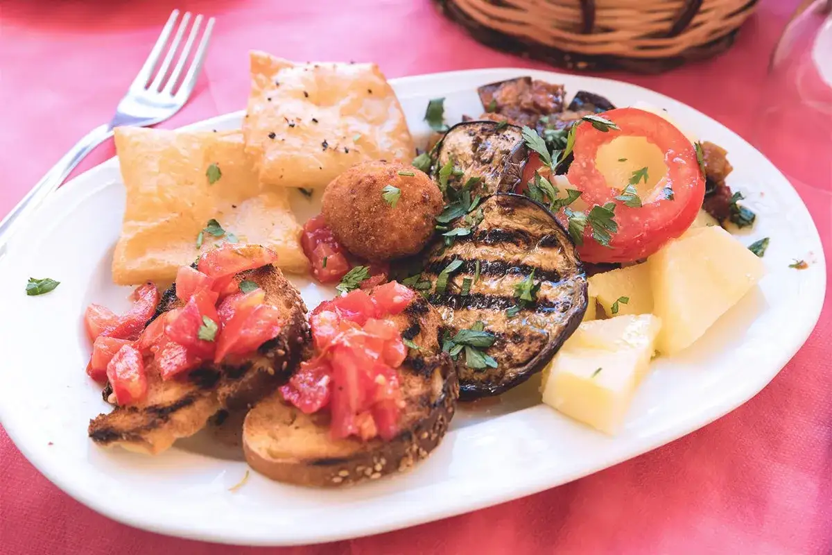 Piatto di antipasti siciliani con bruschette al pomodoro, melanzane grigliate, arancino, formaggio e frittelle.