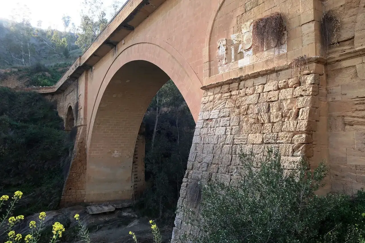 Il maestoso ponte Capodarso, con i suoi archi in mattoni e la base in pietra, domina la vegetazione lussureggiante.